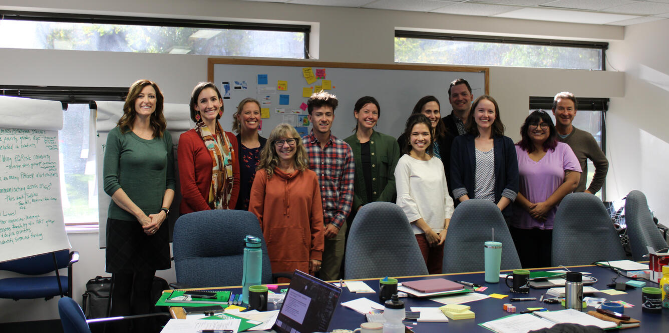 group of 12 people in a room in front of a white board