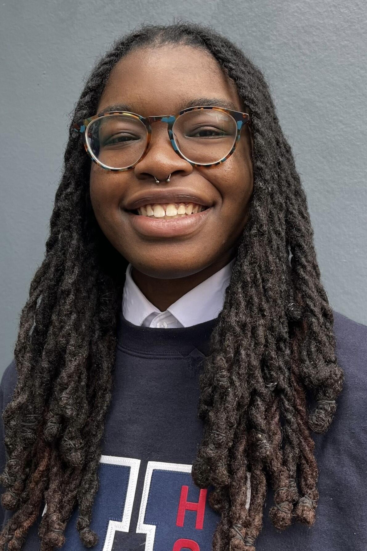Photo of a person with long dark hair wearing glasses in a blue sweatshirt 