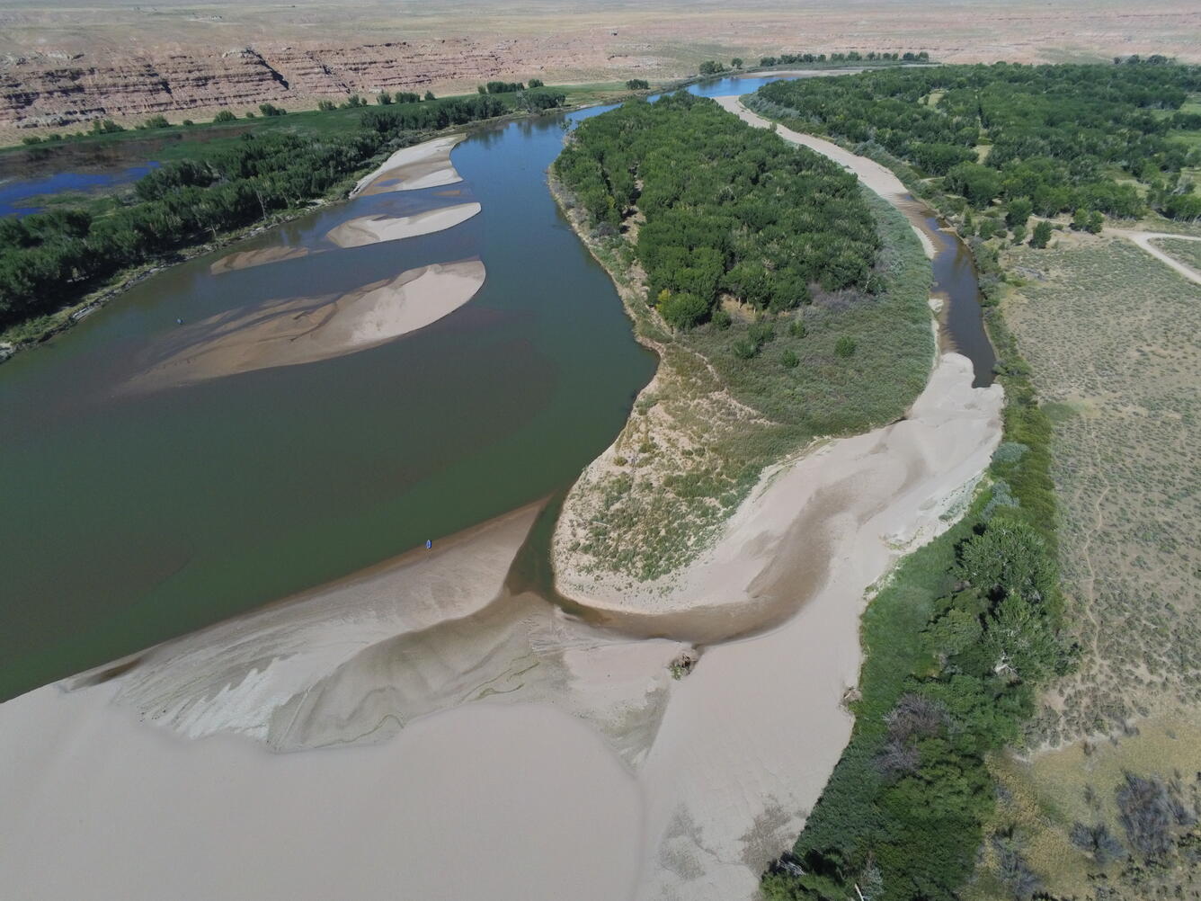 a blue-green river with many sand bars and beaches surrounded by trees and rock formations