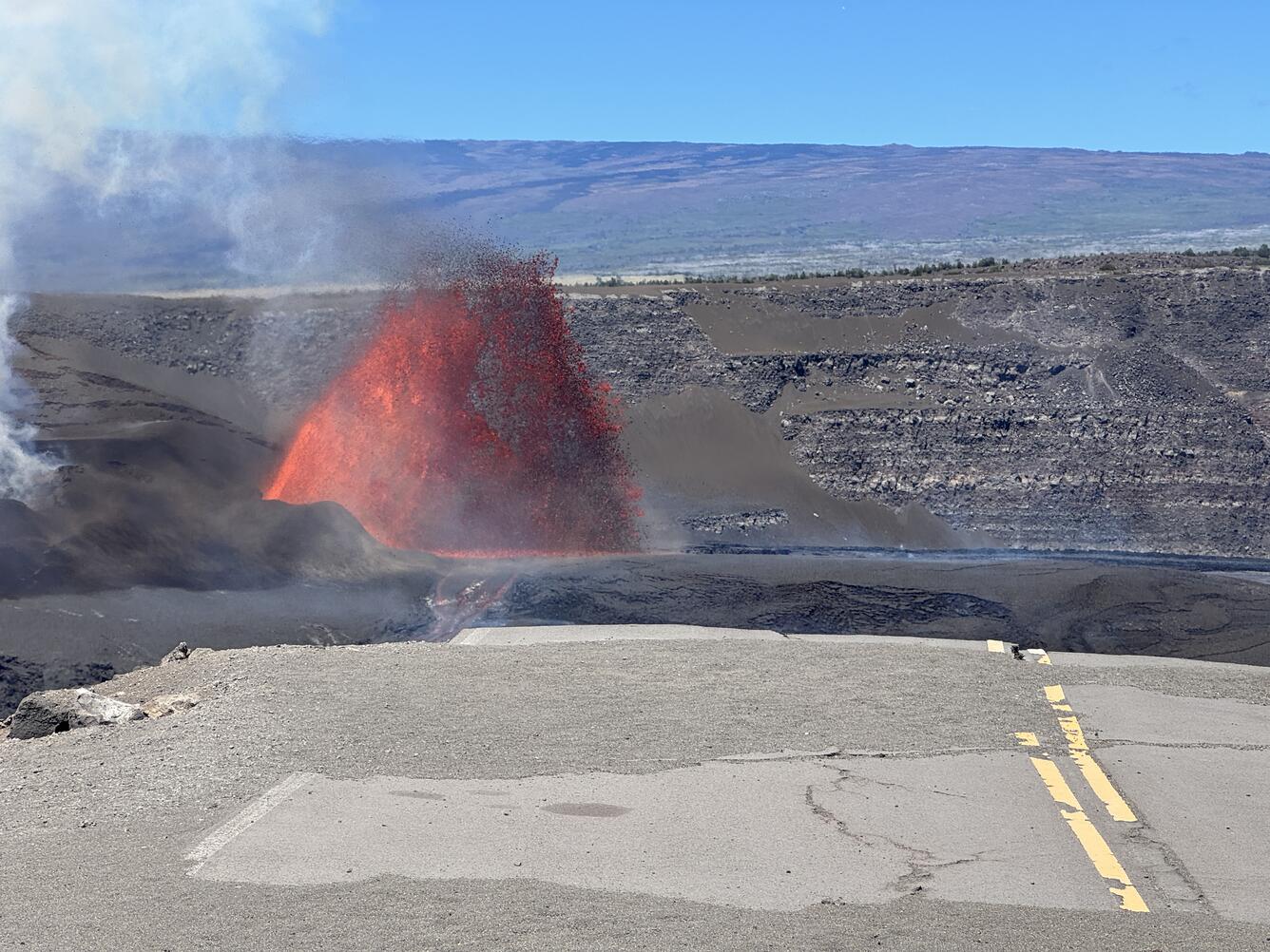 color photo of lava fountain visible beyond the end of a broken road.