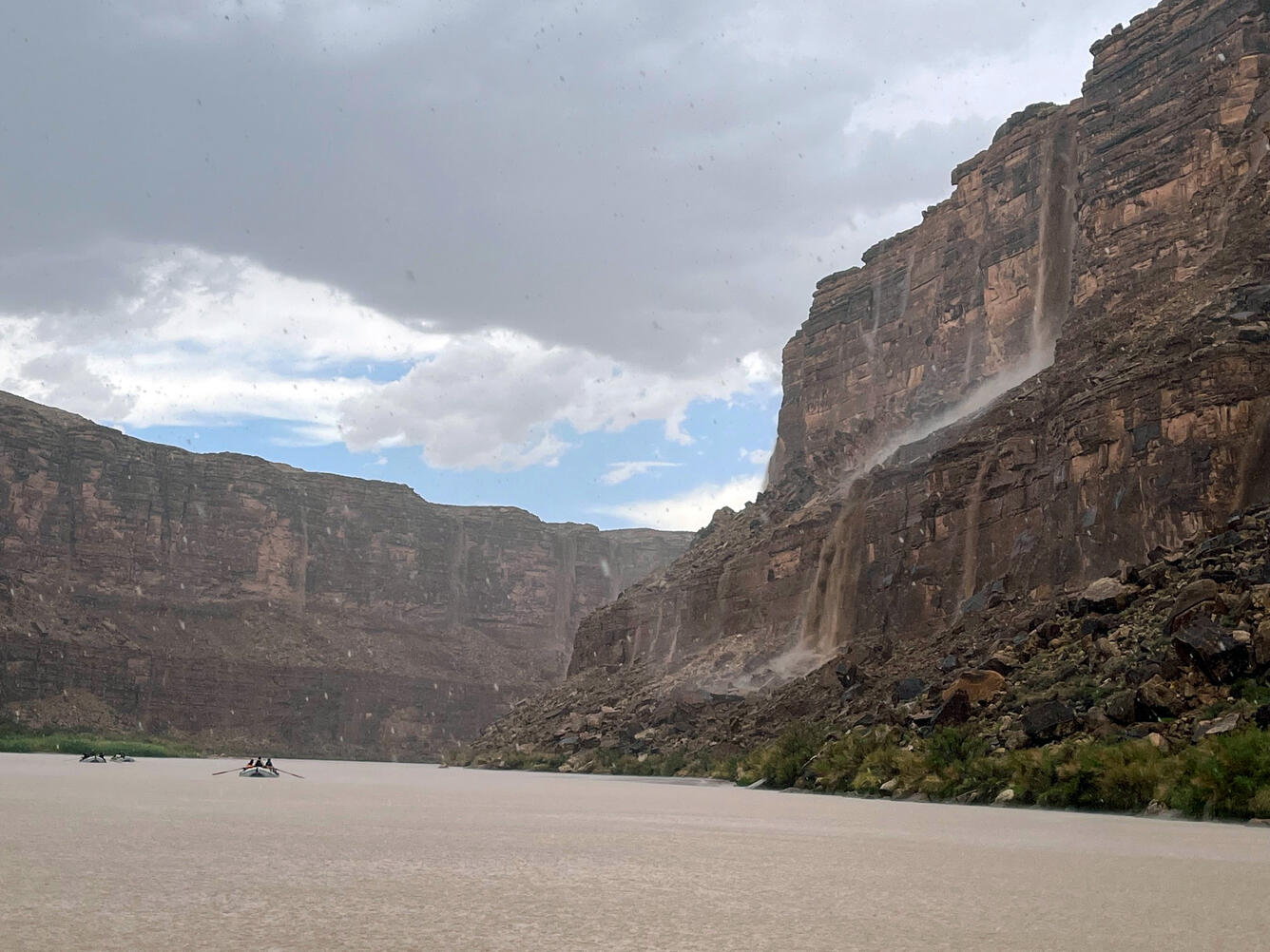 Boats on the muddy Colorado River observe waterfalls and debris flow down Marble Canyon's cliff walls in a rainstorm
