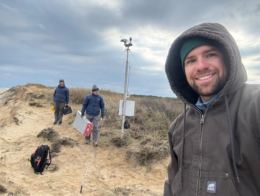 Three people on beach with camera mounted on tall pole