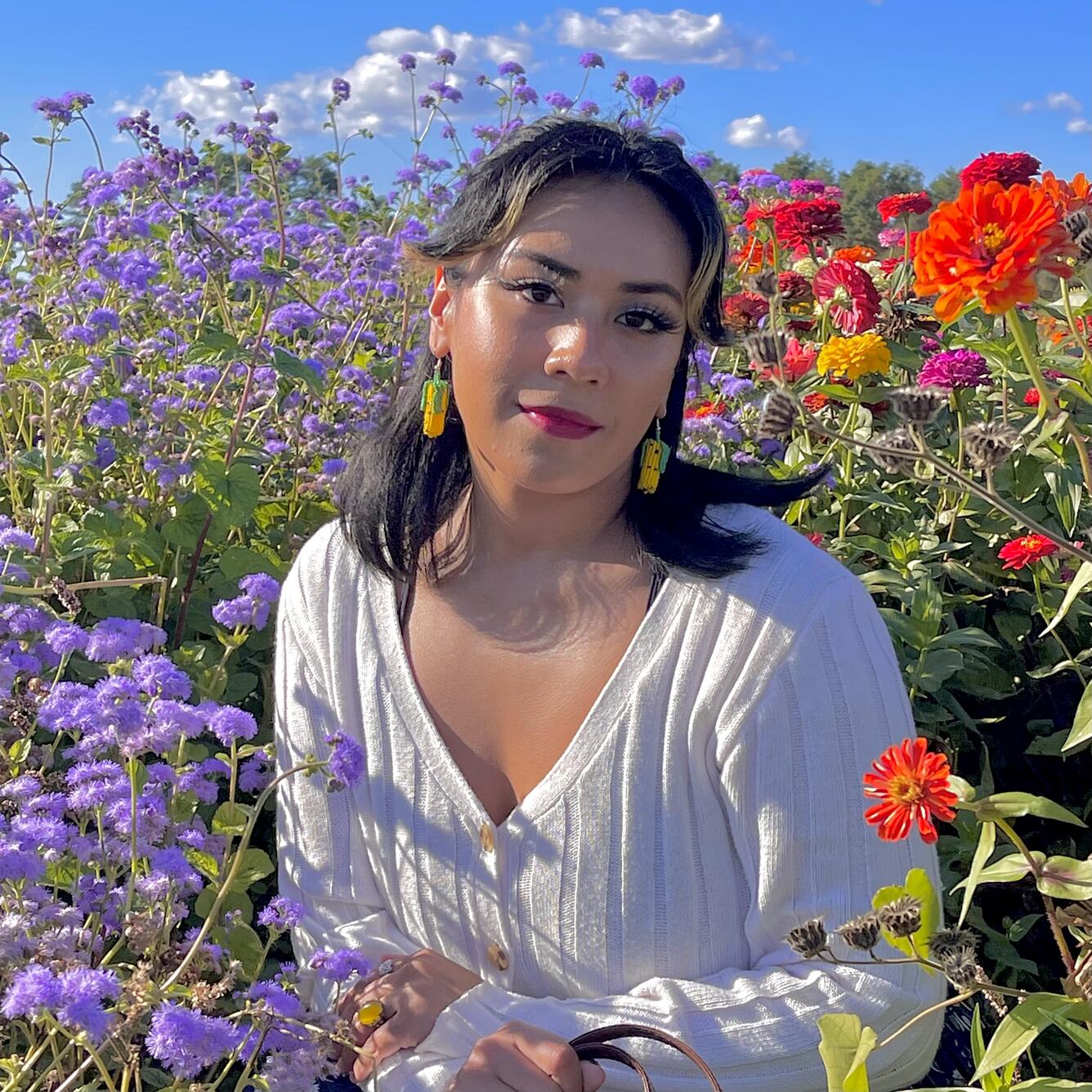 A woman with dark hair stands in a field with tall wildflowers.