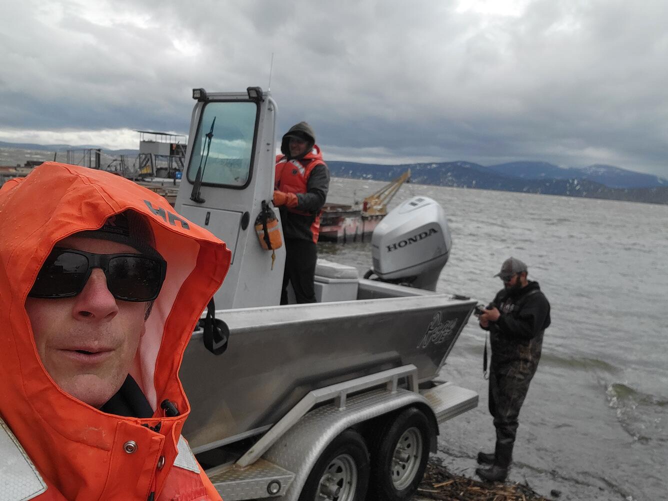 Selfie with man in orange hood and boat with two men in background on Upper Klamath Lake, Klamath Falls, OR
