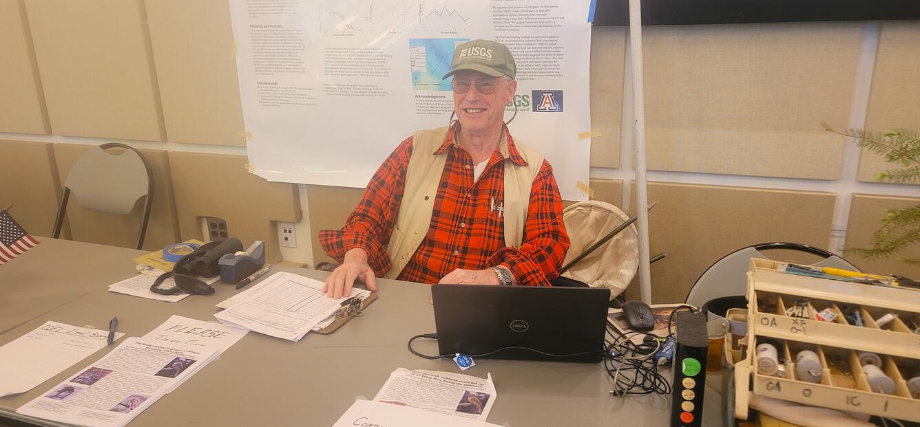 Charles van Riper sits behind a table conducting outreach on Cordilleran Flycatchers at an event on Mt Lemmon, Tucson, AZ