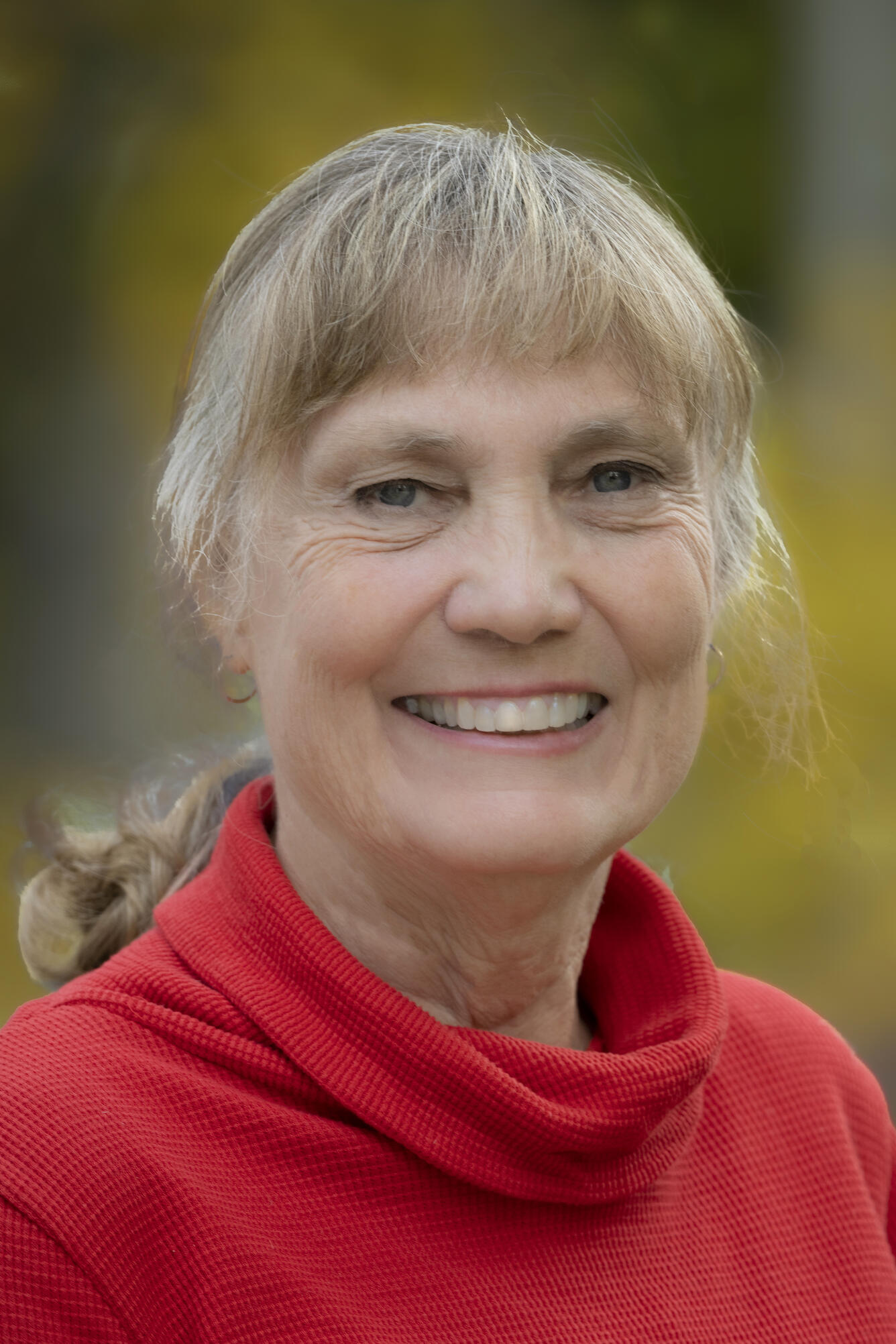 Head shot of Kristin McDougall-Reid. She is smiling and wearing a red shirt. Her blond and gray hair is pulled back in a low ponytail.