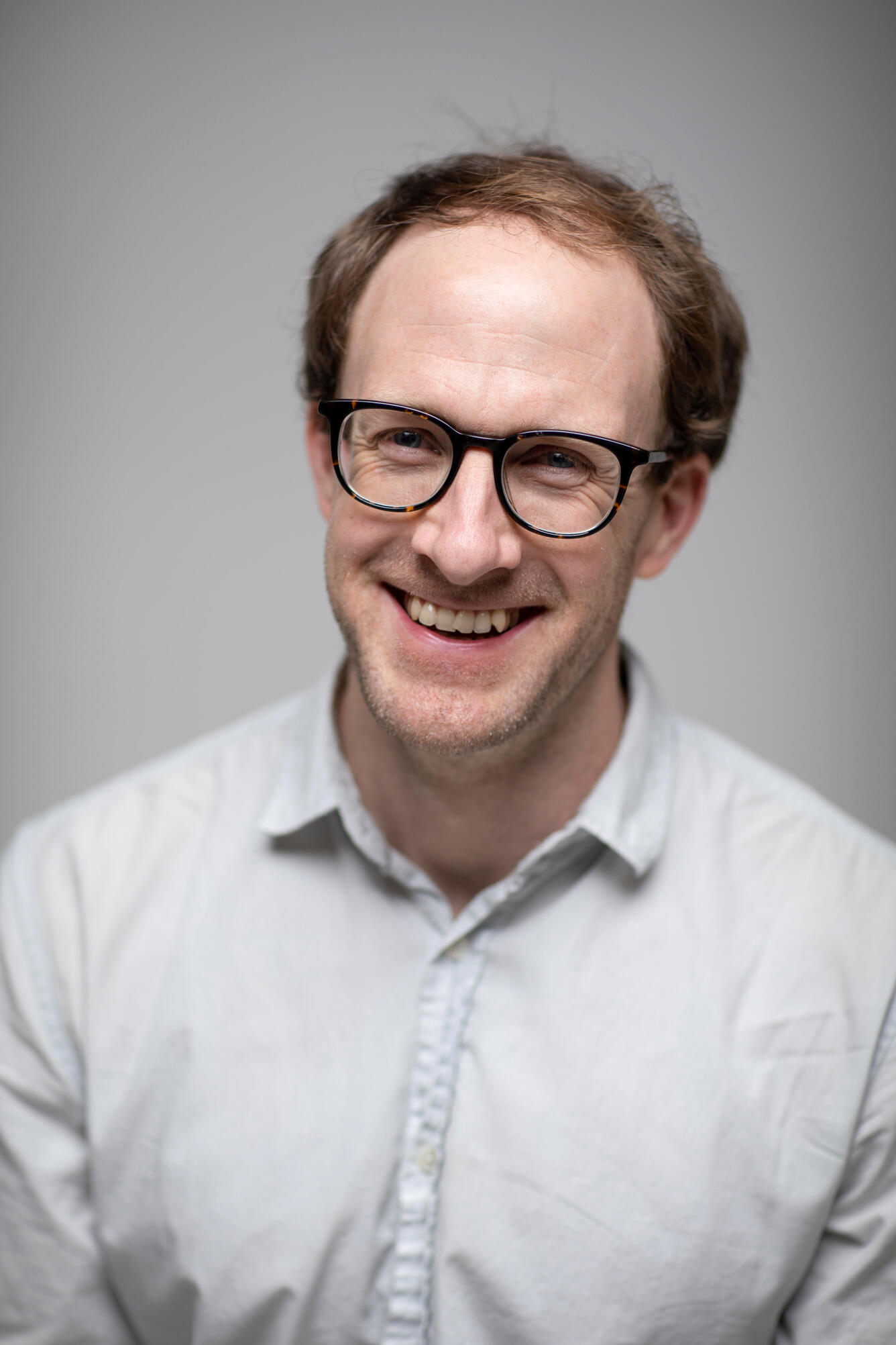man smiling, wearing glasses and a white shirt