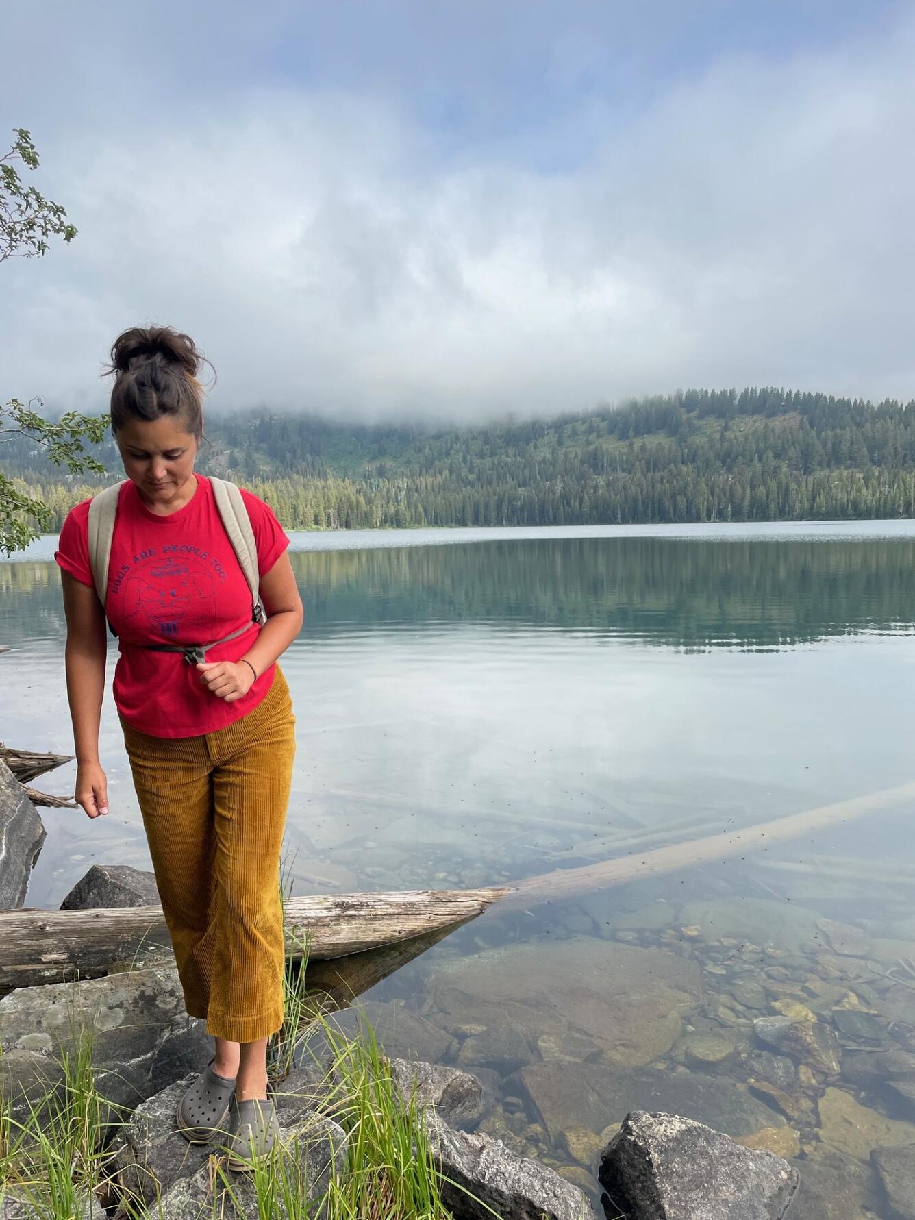 woman in red shirt looking down with sky behind her
