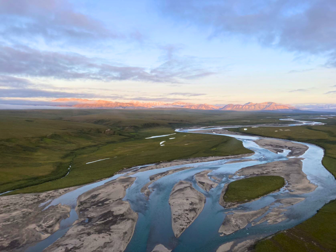 An aerial view of a river surrounded by green hills, with a mountain range in the distance.