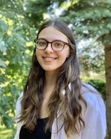 A smiling woman with long wavy dark blonde hair wearing glasses.