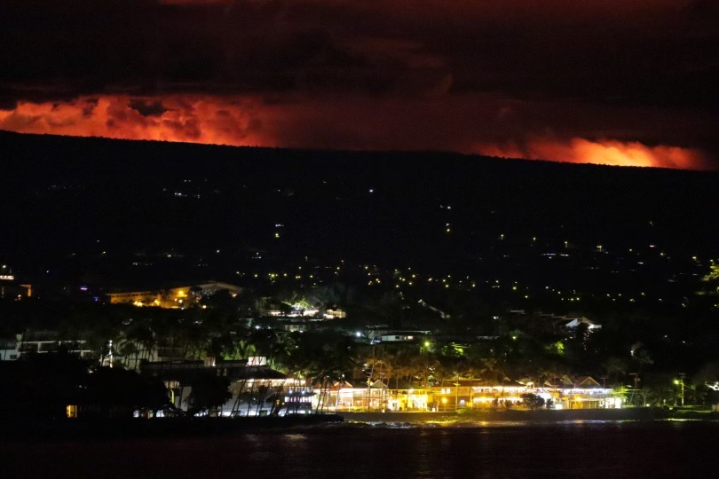 Color photograph of glow from volcanic eruption lighting the night sky above a town