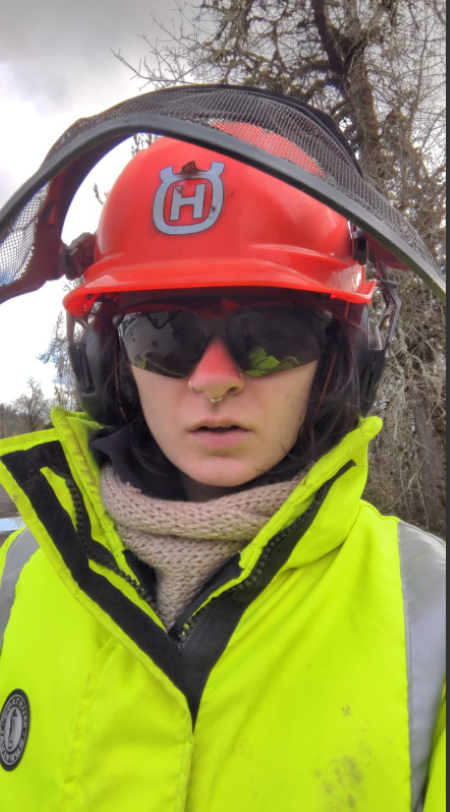 Jillian Garsjo is wearing a bright yellow rain coat, safety goggles, and red hat hard hat with net shield. 