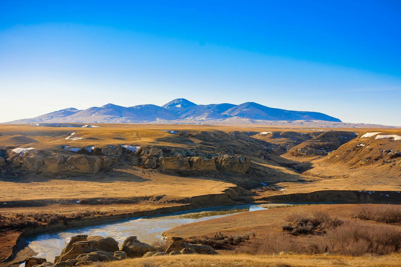 An image of the Milk River with chunks of ice floating down it. Bluffs stand in the background.