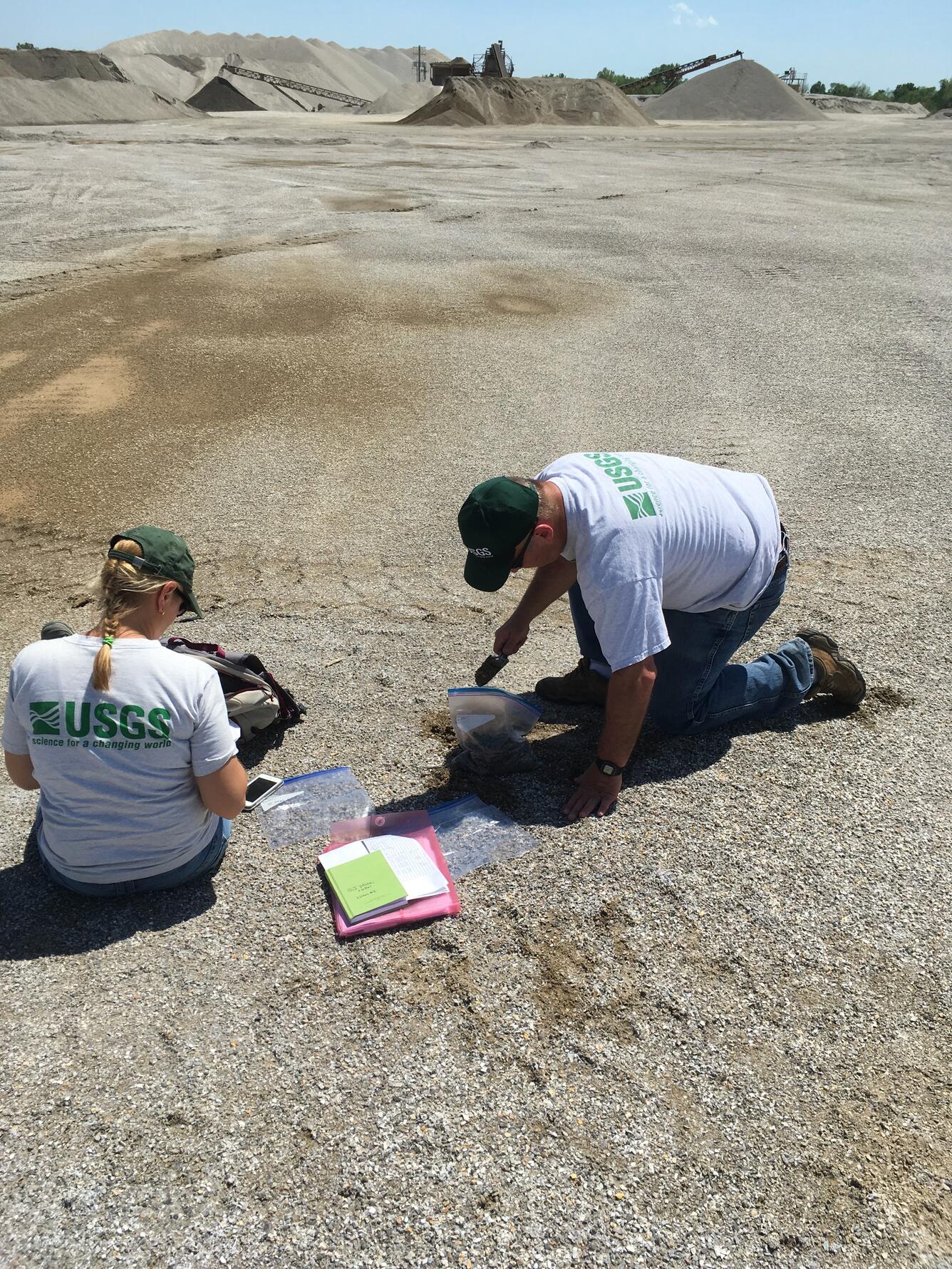 Two scientists in USGS gear examine a field of seeming pebbles.