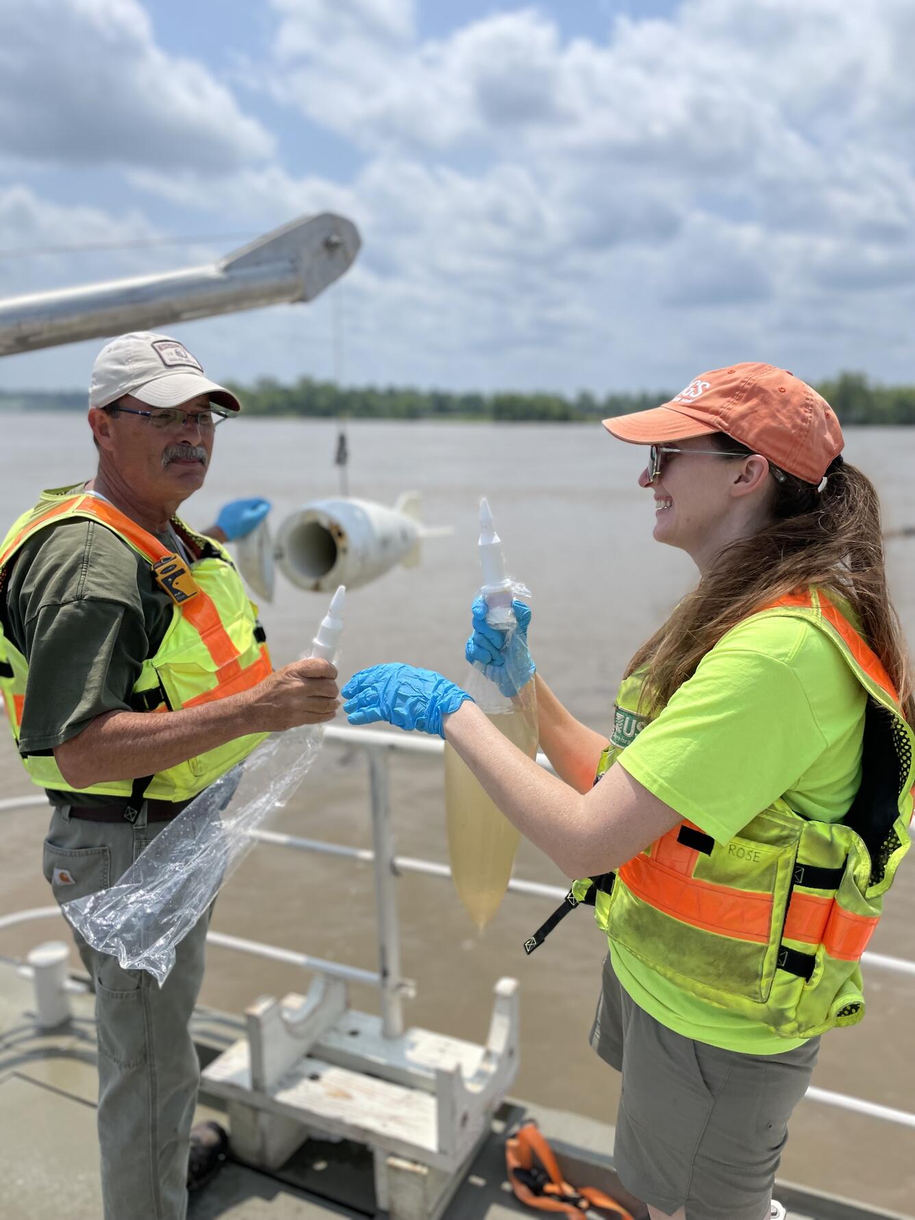 Two scientists stand on dock next two river holding water samples.