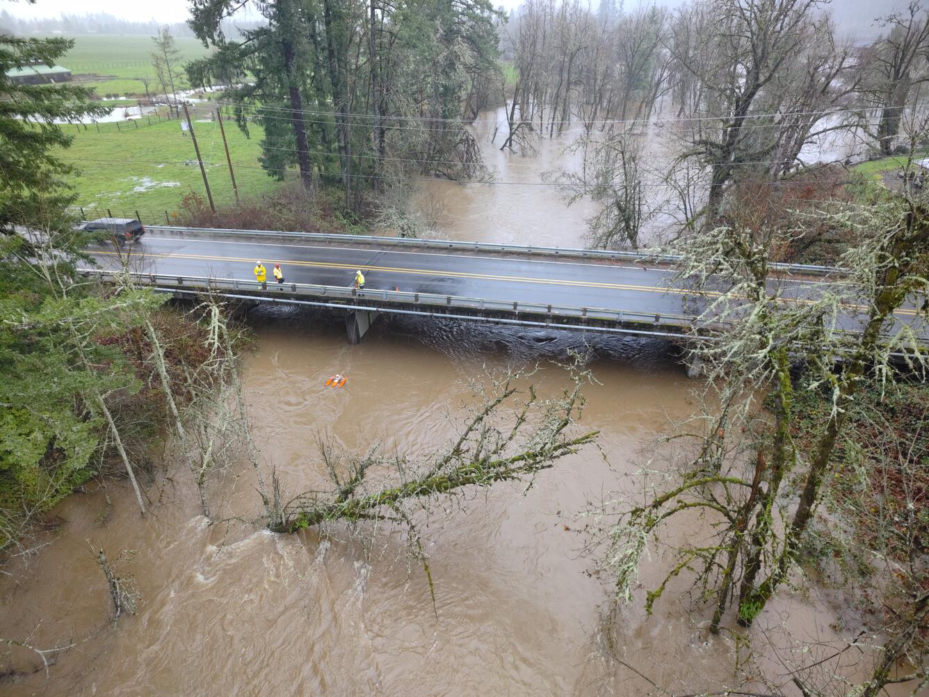 high up view, field crew are small brightly colored figures standing on a bridge while measuring