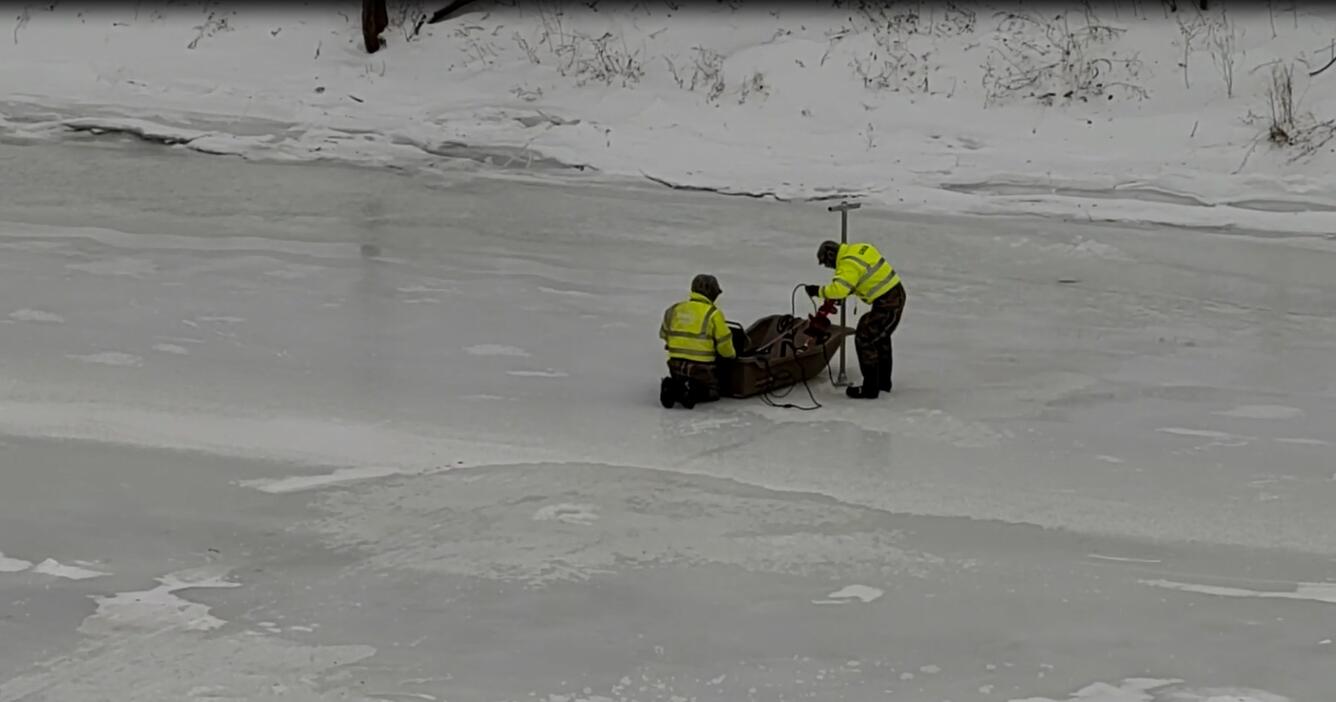 USGS Scientist standing on the frozen river lower equipment into the waters below through a hole in the ice