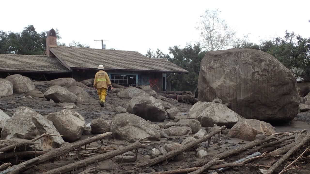 Large boulders and person walking in front of damaged house