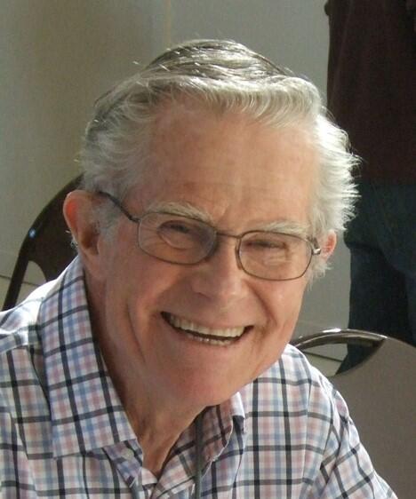 Headshot of a white-haired man wearing glasses, smiling broadly