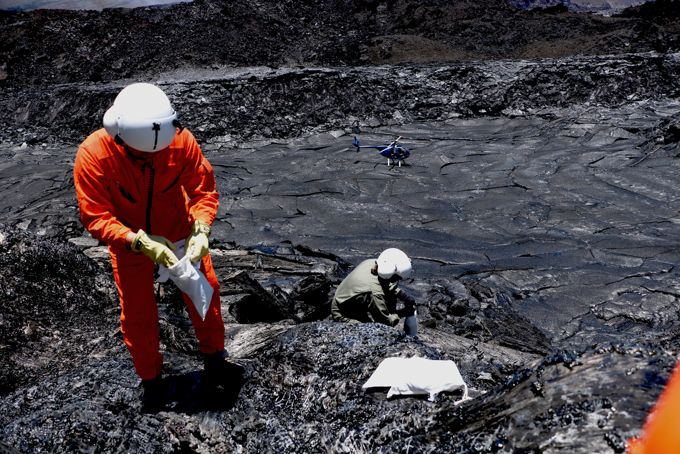 Color photograph of two scientists collecting a sample of spatter from the now cooling episode 30 eruption.