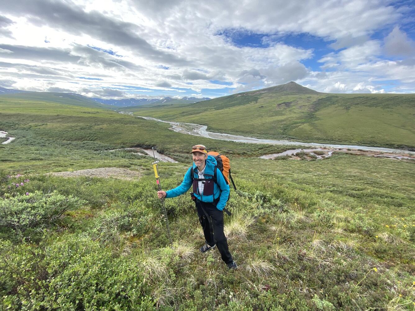 A man in a blue jacket standing in front of a river.