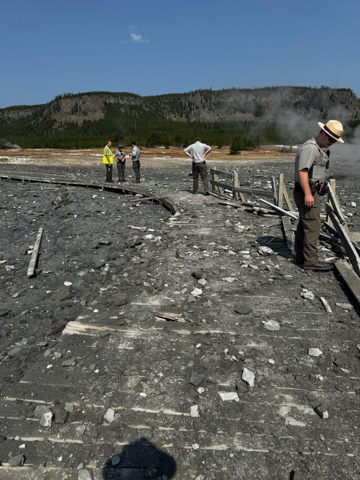 Workers stand on a pathway covered in large stones and rocks, almost unwalkable.