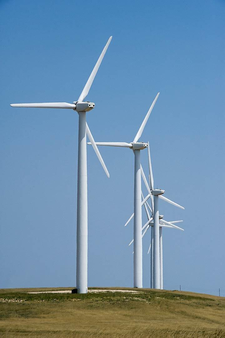 Several wind turbines along a grassy stretch of land under a clear blue sky