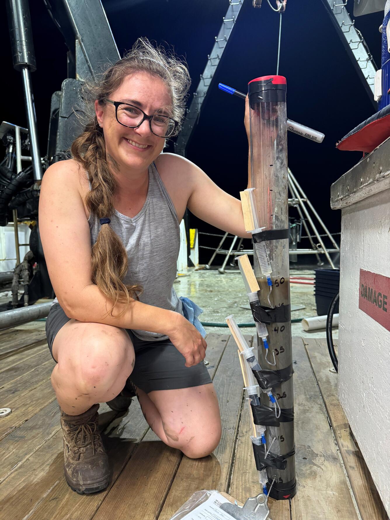 Person kneeling next to core sample on deck of ship at night
