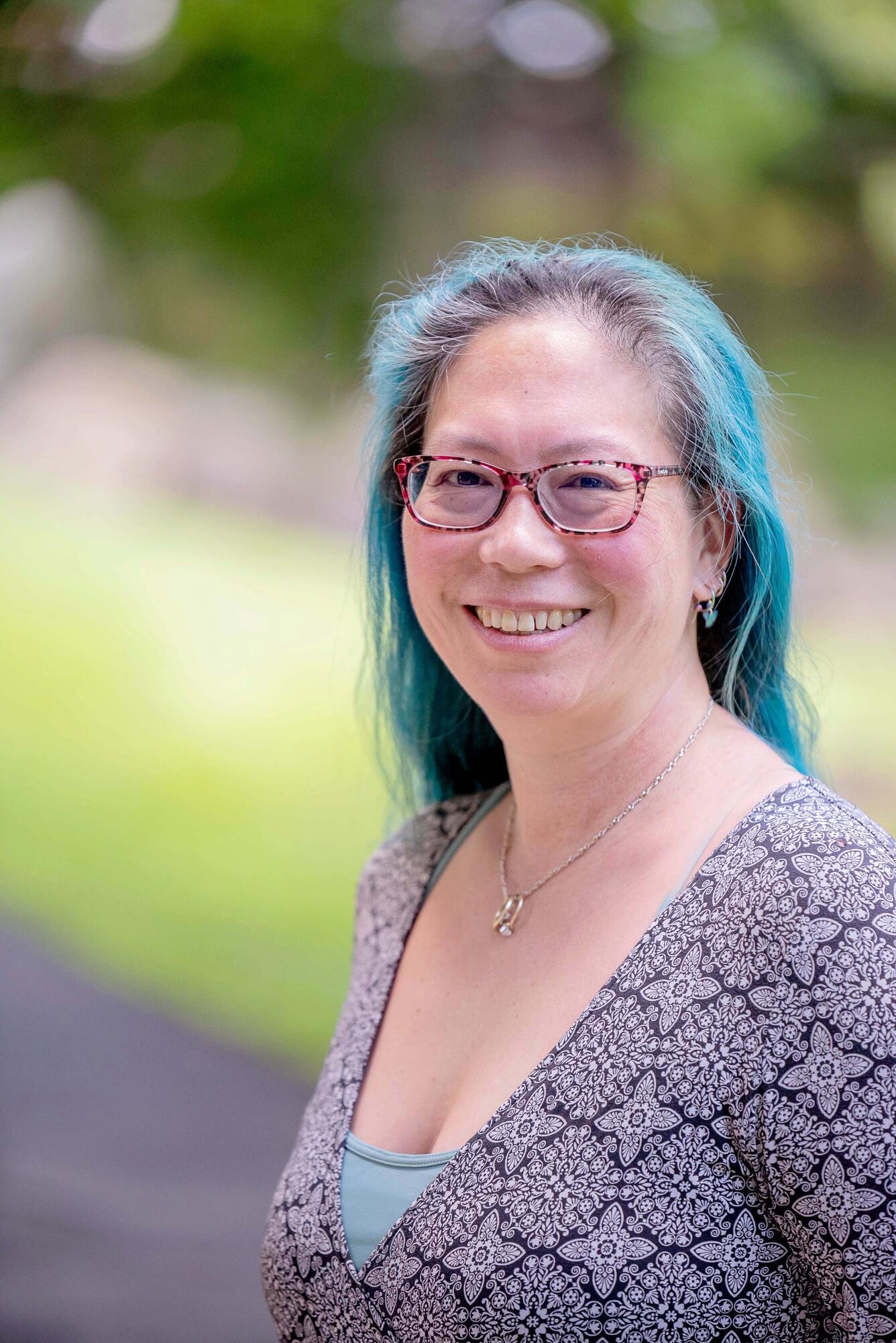 headshot of sue kemp, a person with long blue hair wearing glasses