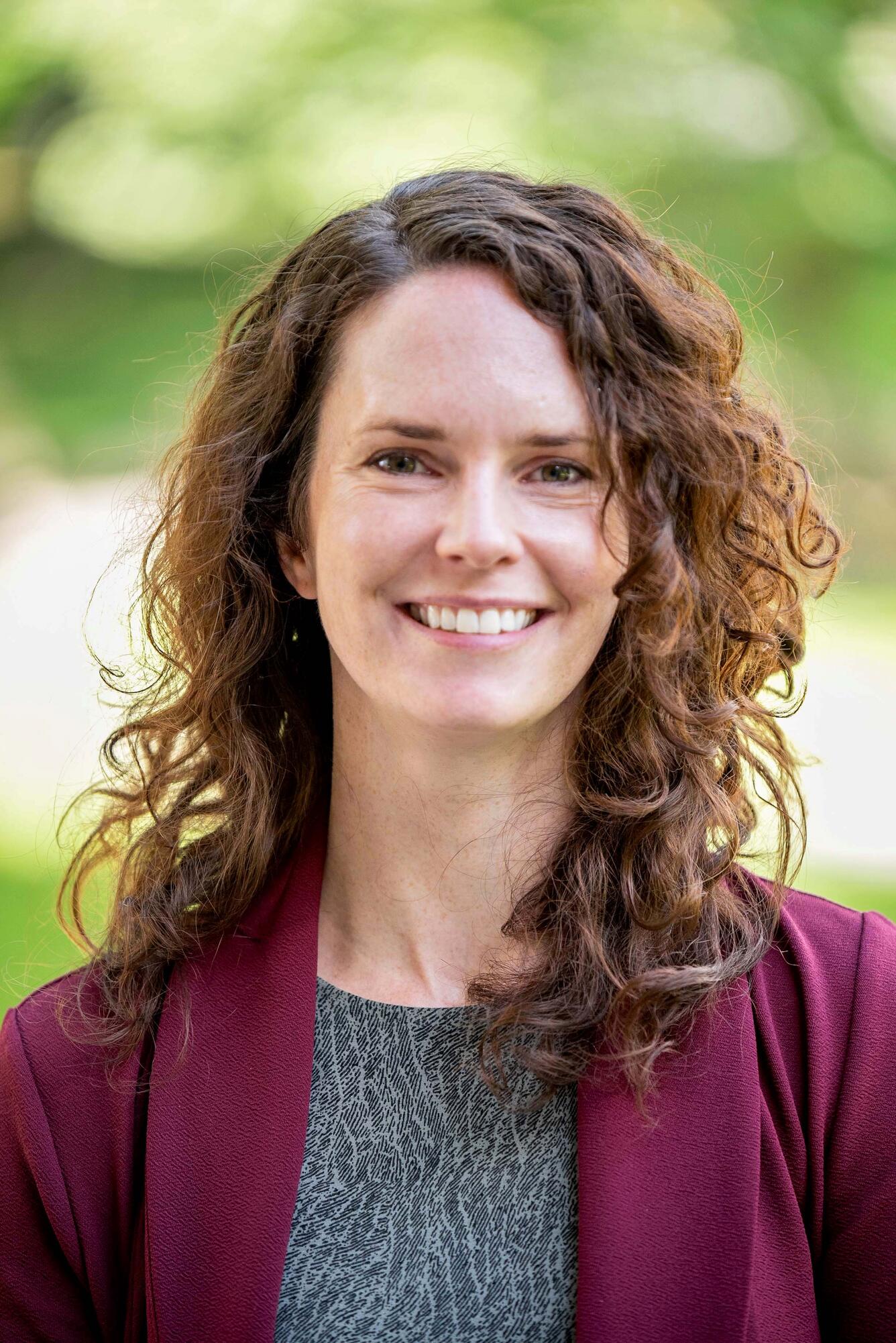 headshot of rachel powers, a person with long curly red hair standing outside