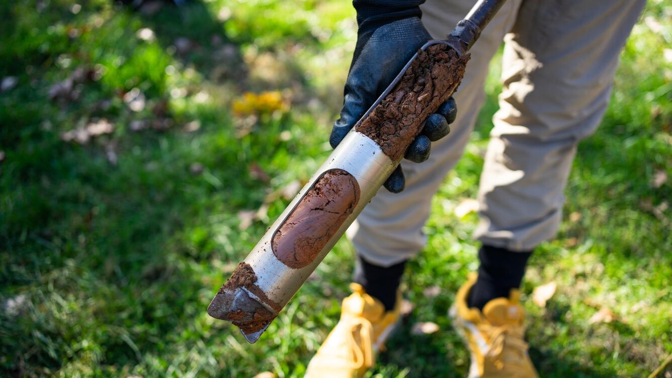 A scientist holds a cored sediment sample in a park.