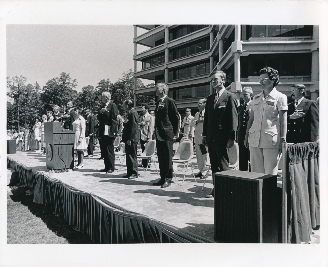 A black and white photo of a group of leaders and presenters, dressed in suits, outside in front of the building.