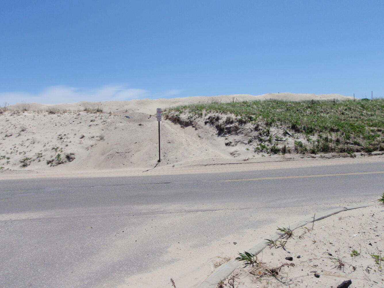 A dune that has sand washed over it next to a road during a storm