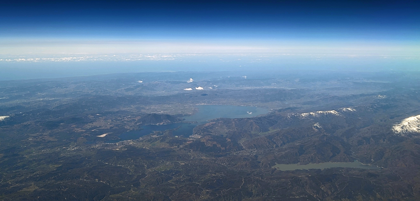 A photo taken from an airplane of a large, elongated lake surrounded by long mountain ridges and vineyards