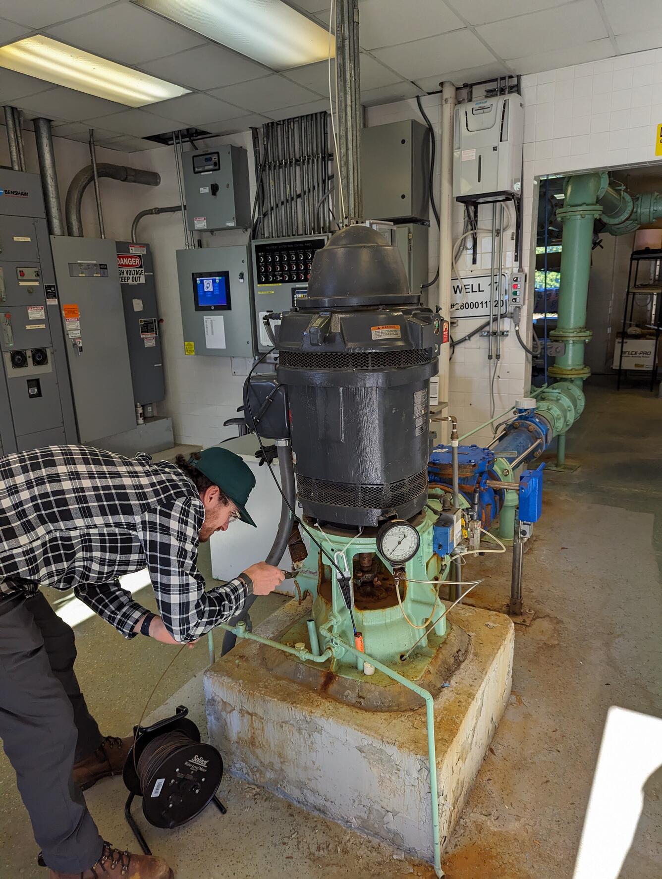 Man bent over lowering a measuring tape into an access pipe in a groundwater pump