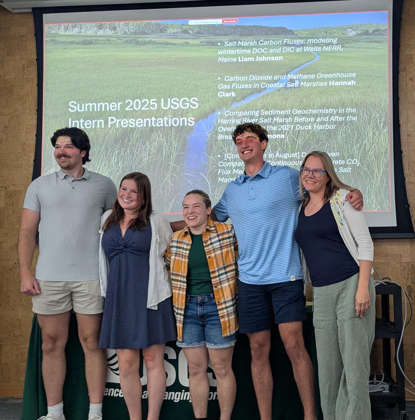 four people posing for photo together in front of PowerPoint presentation