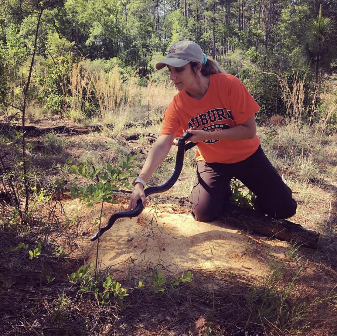 photo of a woman holding a snake, trees in the background