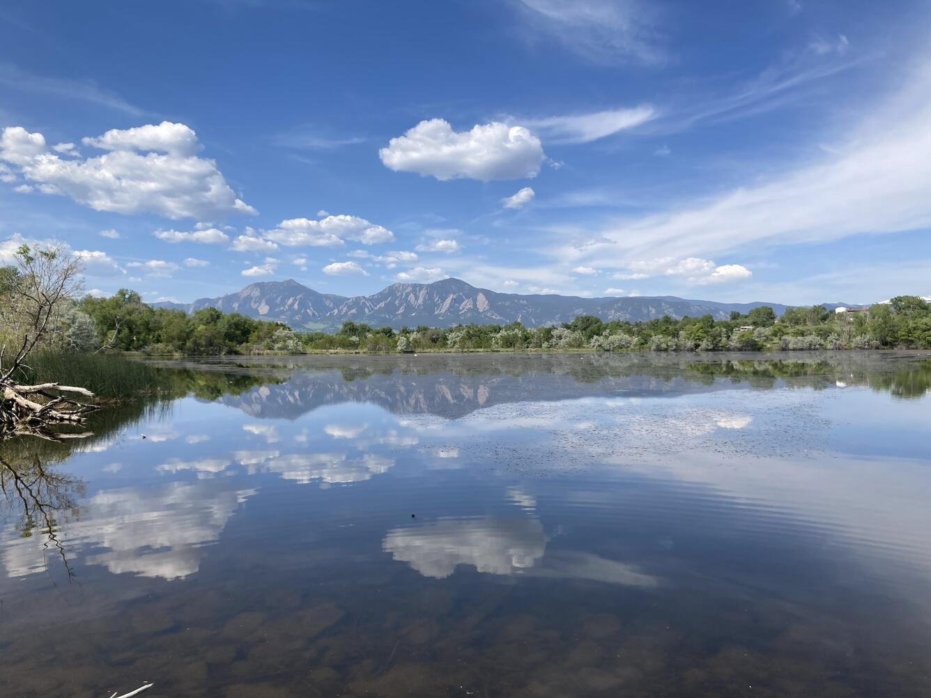 Landscape view of body of water surrounded by green vegetation with mountain, blue sky and white clouds in the background