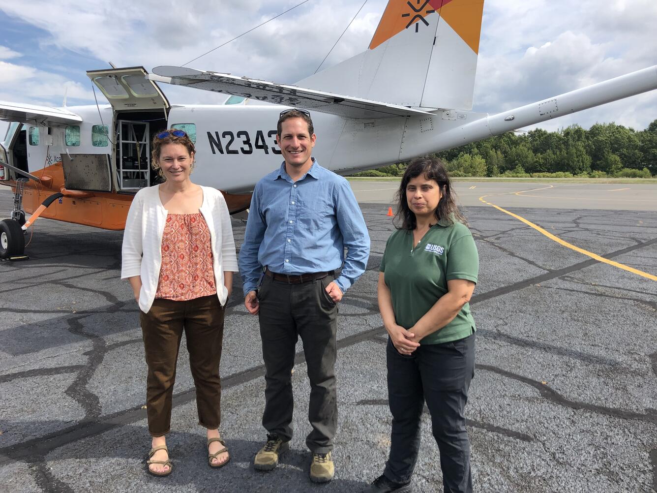 Three people standing on tarmac in front of a survey aircraft.