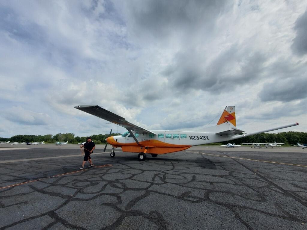 Aircraft on tarmac with dramatic clouds, staff running electrical line.