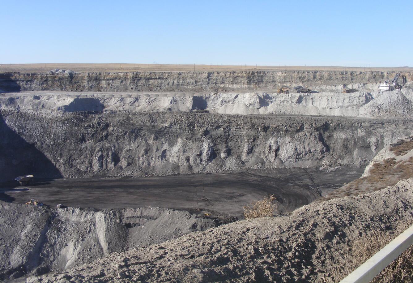 A vast view of an open pit mine with a couple of pieces of equipment in position