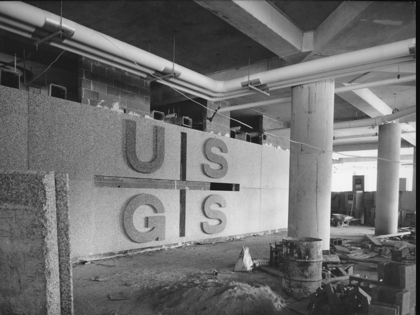 A black and white photo of the incomplete main lobby, with 'USGS' separated by lines into quadrants in stone on the back wall