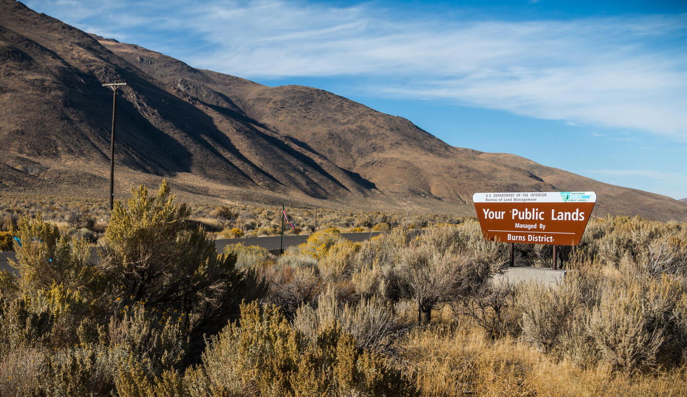 sagebrush landscape with mountains in the background and an entrance sign reading "Your Public Lands"