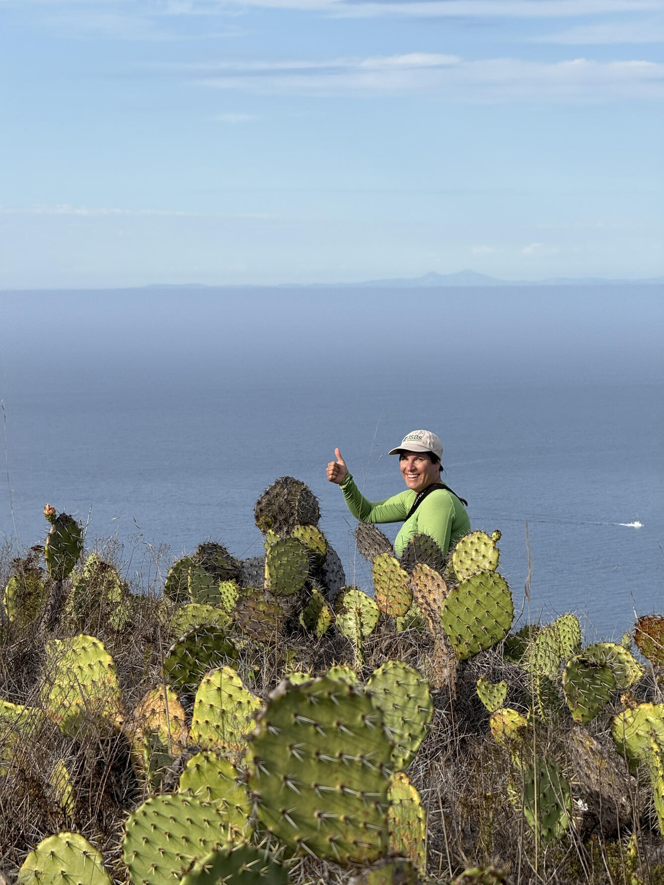 Biologist Sarah Birchard stands near prickly pear cacti and gives a thumbs up at Pyramid Point, San Clemente Island