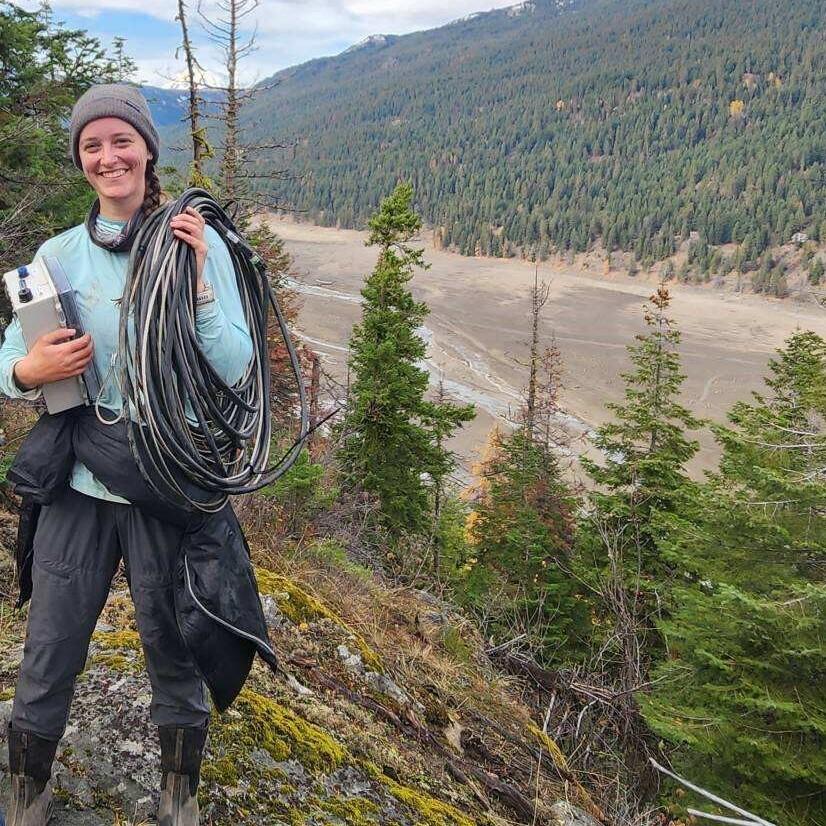 woman carrying rope and box with mountains in background