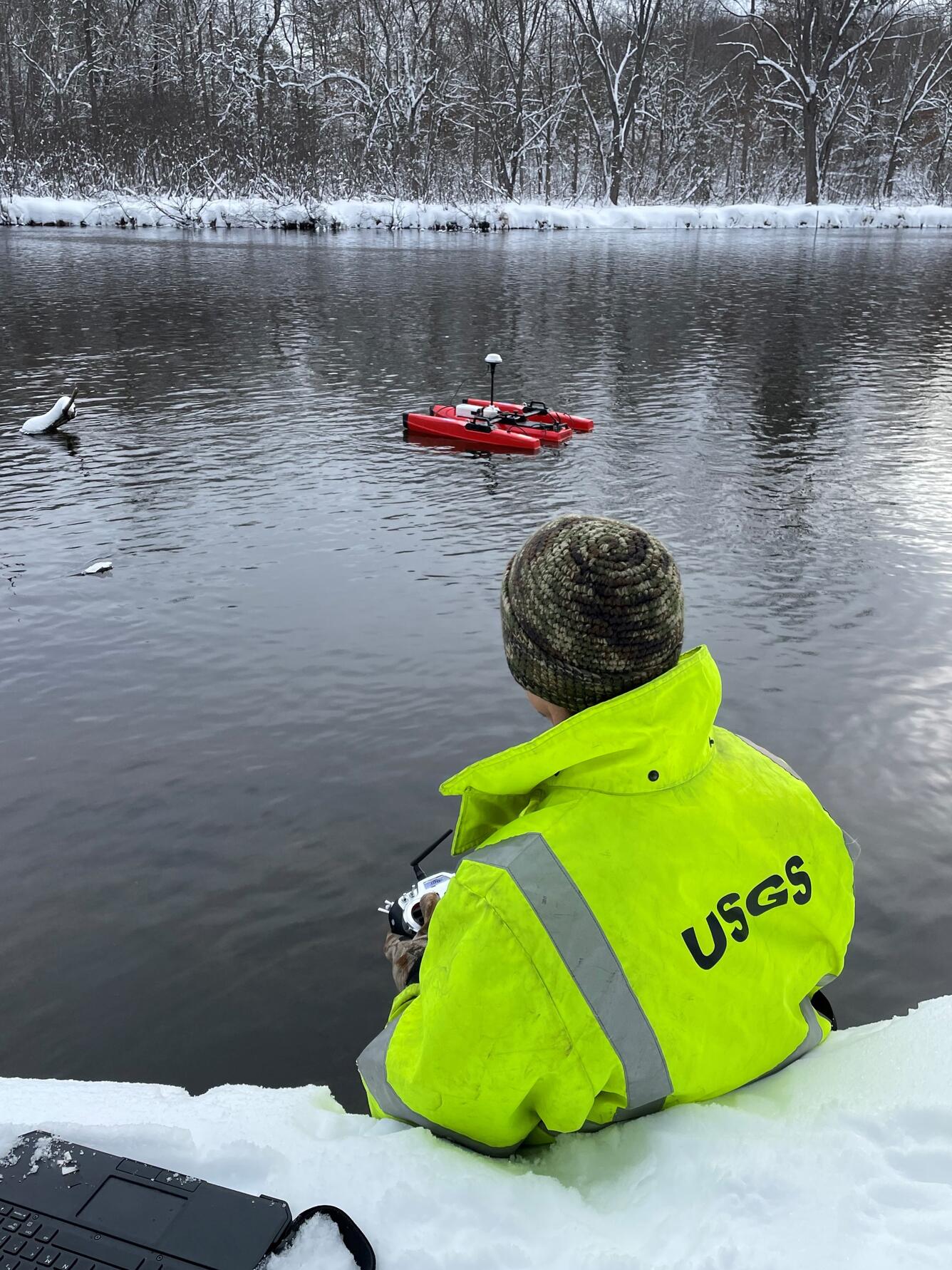 USGS employee making measurement using remote-controlled ADCP in middle of river in winter