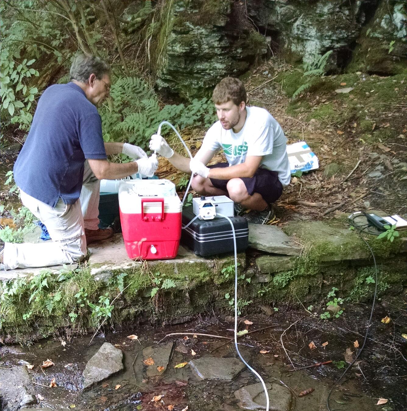 Photograph of two people pumping water samples from a spring