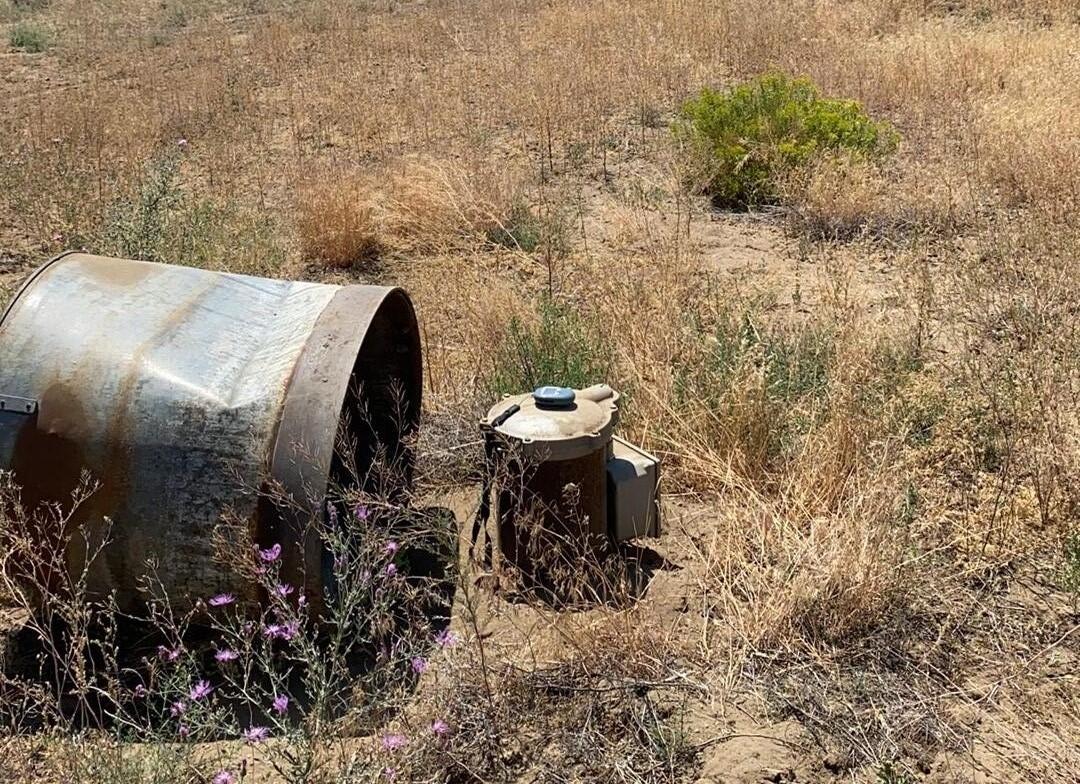 Steele casing and wire proof well cape jutting from the ground in a landscape of dry yellow grass and spare trees, blue skies