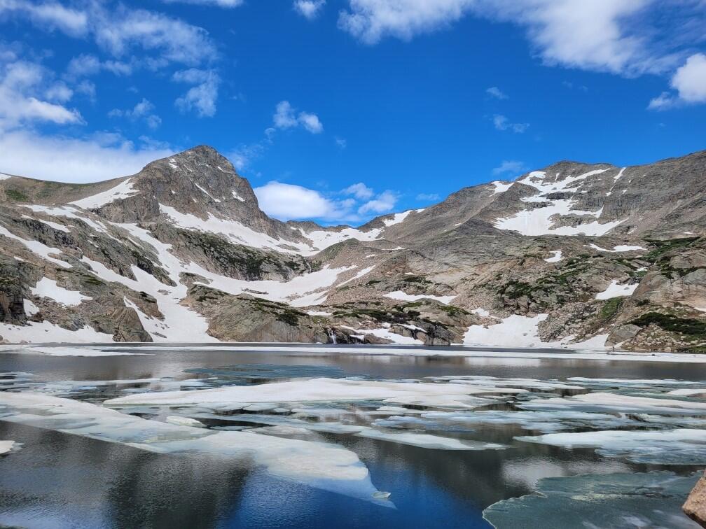 photo of icy lake with bare mountains in background with a little snow