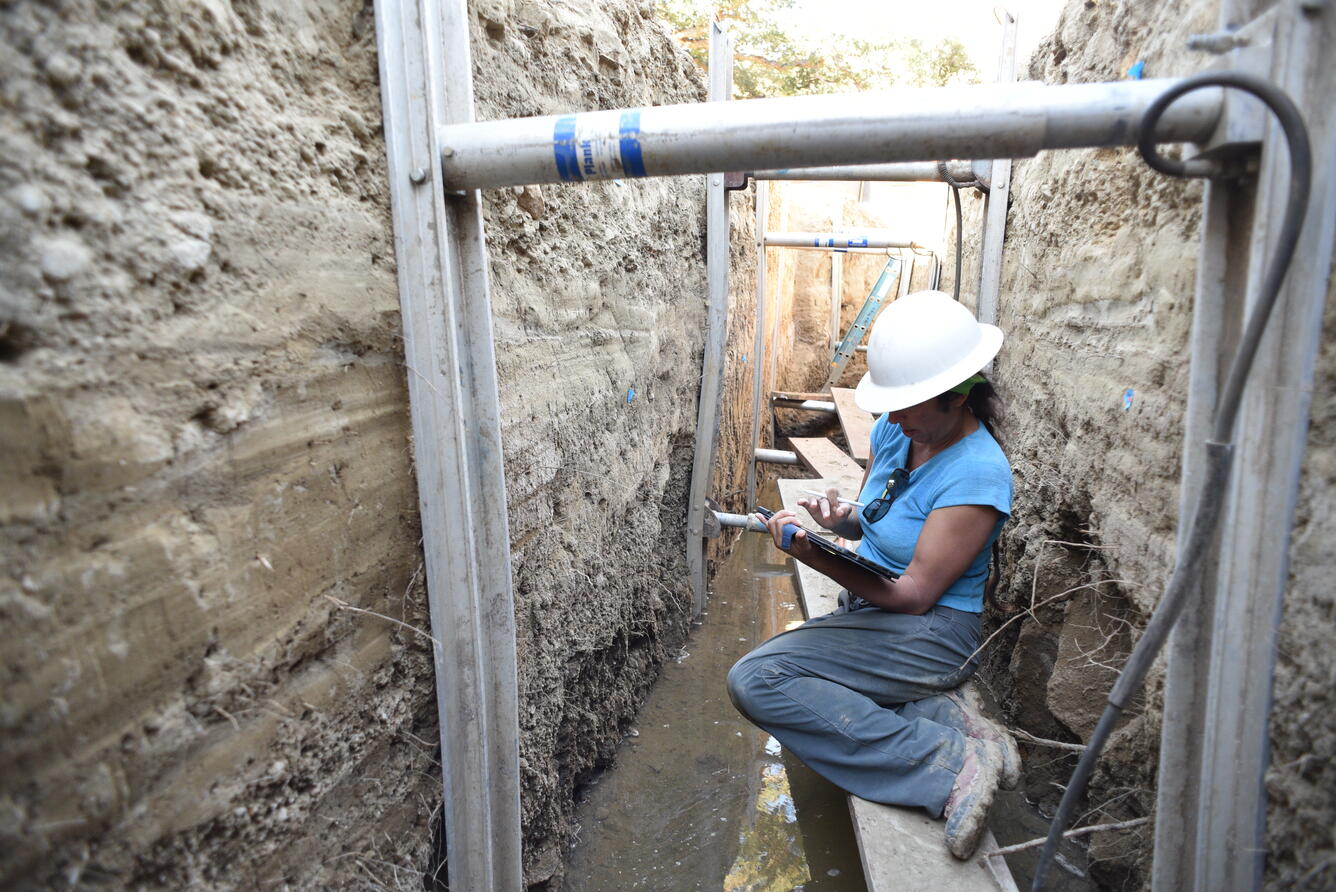 USGS scientist taking notes while seated on scaffolding inside a deep paleoseismic trench cut into the San Andreas fault.